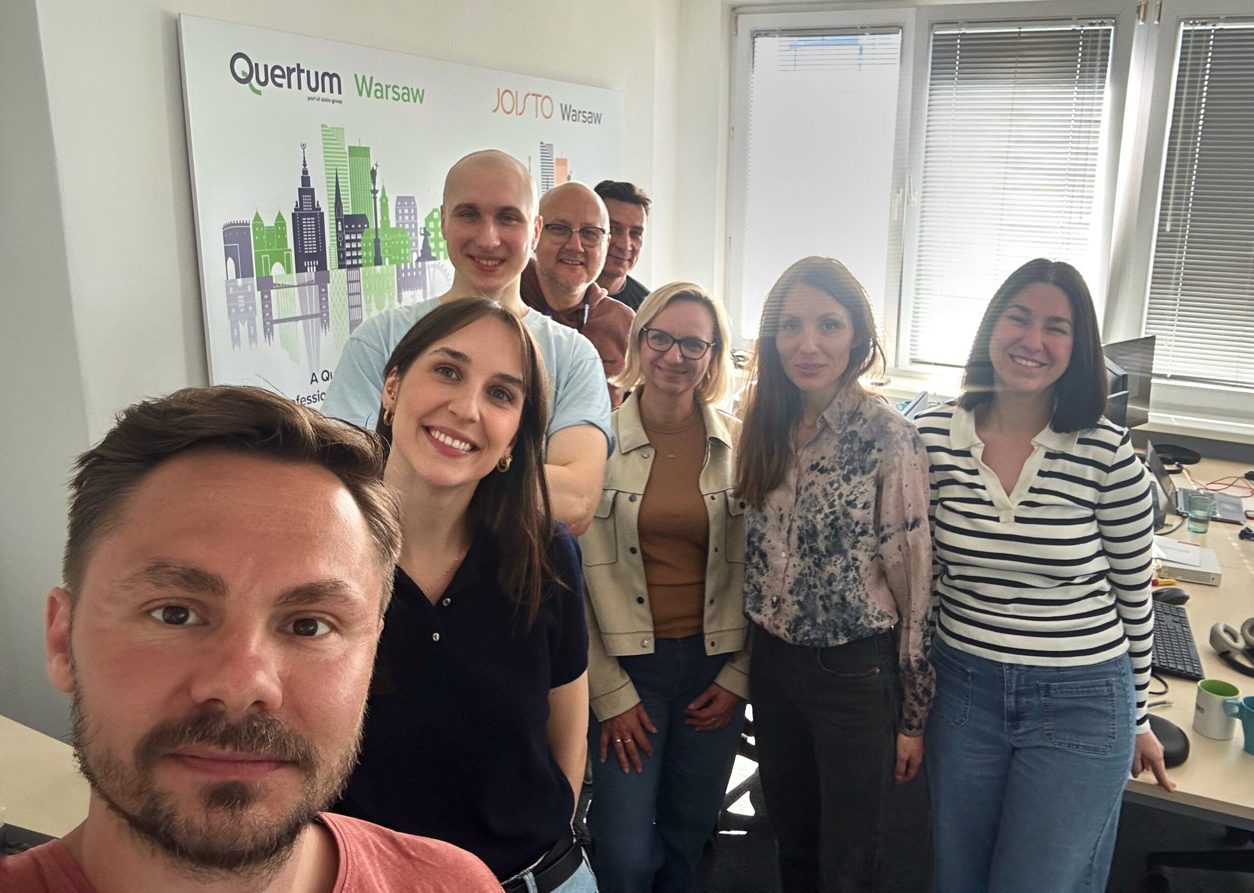 Le directeur général se tient avec son équipe dans le bureau, avec le panneau Quertum en arrière-plan.