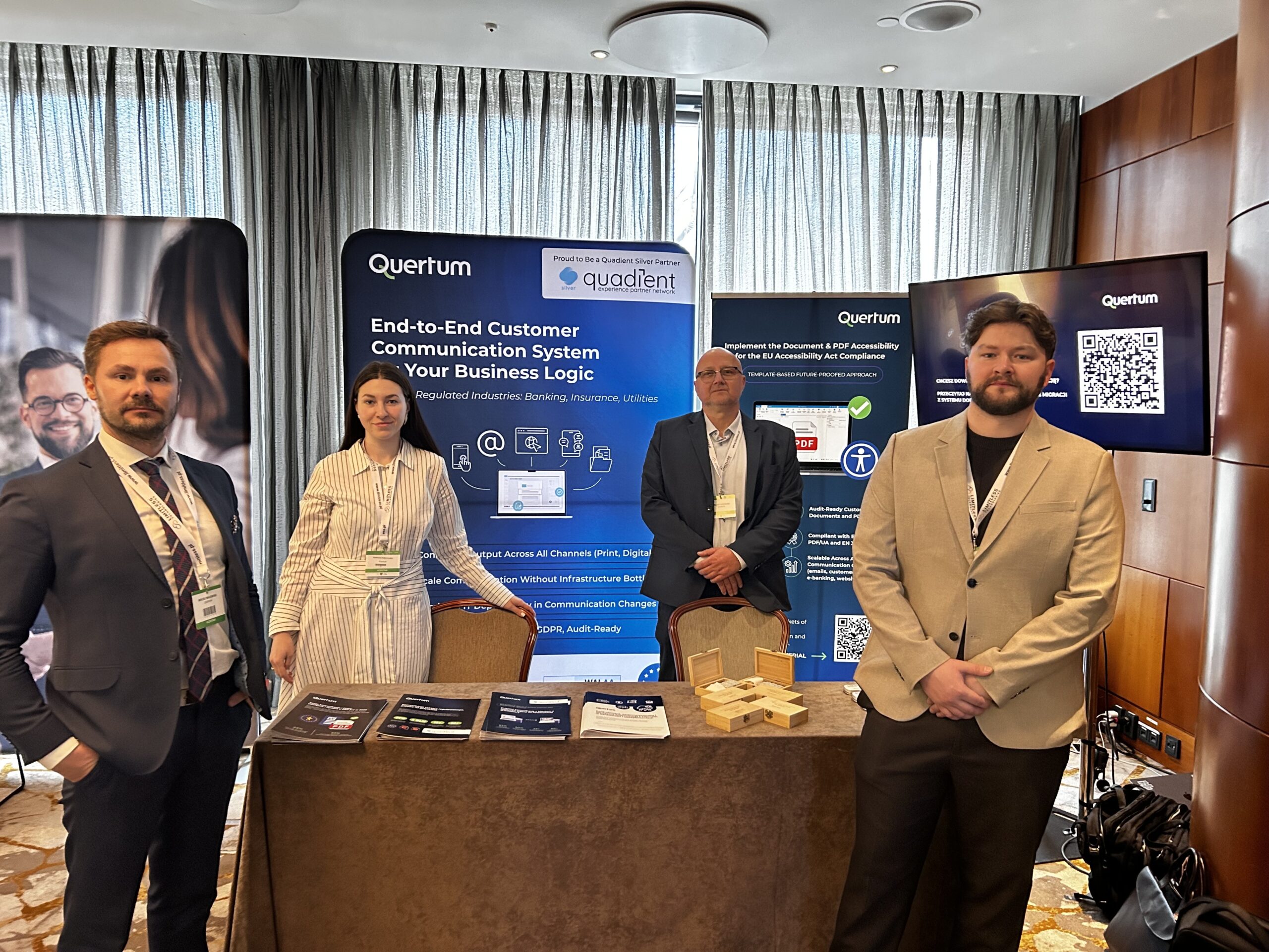 Maciej Majewski, the CEO, Kateryna Kalynovska, the Marketing Executive, Leszek Boniecki the sales Representative and Łukasz Szczepański the CTO are next to Quertum booth and roll-ups of Quertum services. Photo on the tradeshow event.